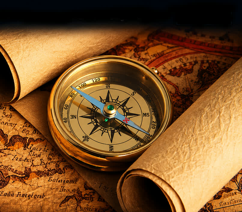 A brass compass resting on antique maps and rolled parchment scrolls
